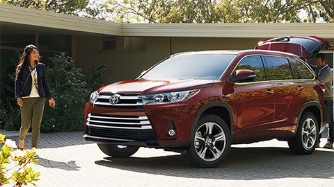 A family standing next to a red Toyota Highlander with the trunk open, parked in a modern driveway.